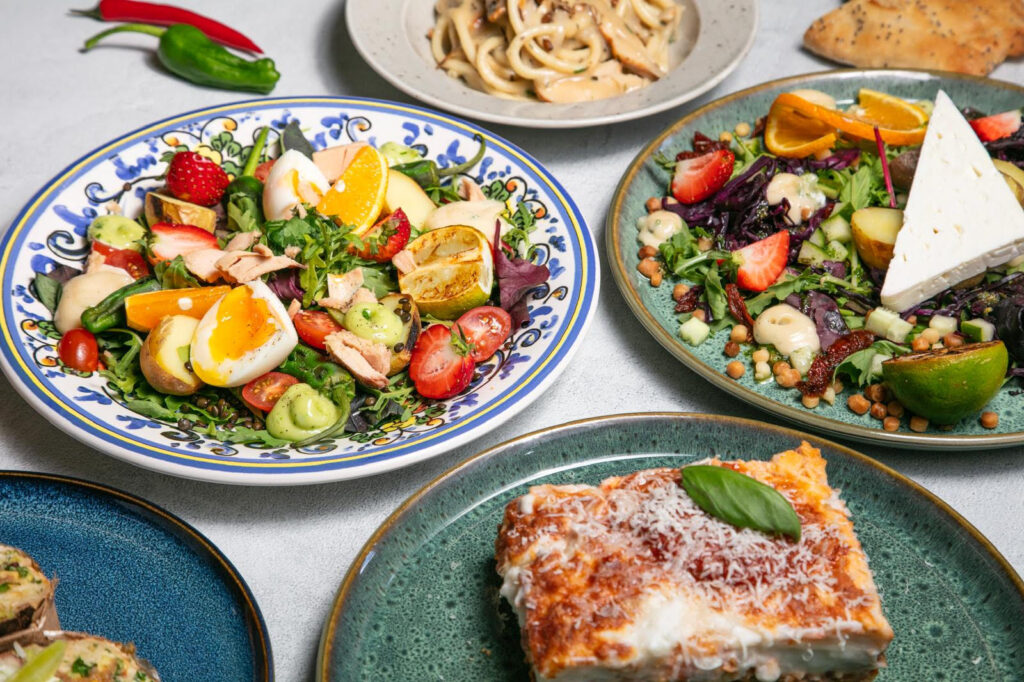 hälsosamma matlådor med fräsch sallad, ägg, lax, jordgubbar och rostade grönsaker, en tallrik med lasagne toppad med parmesan, och en sallad med fetaost, kikärtor och citrusfrukter.